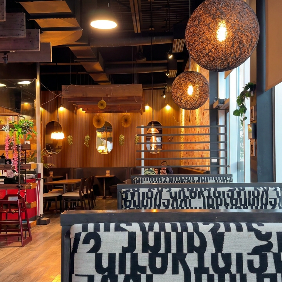 Warmly lit restaurant interior with wood walls, patterned booths, hanging globe lights, dining tables, and floor-to-ceiling windows.