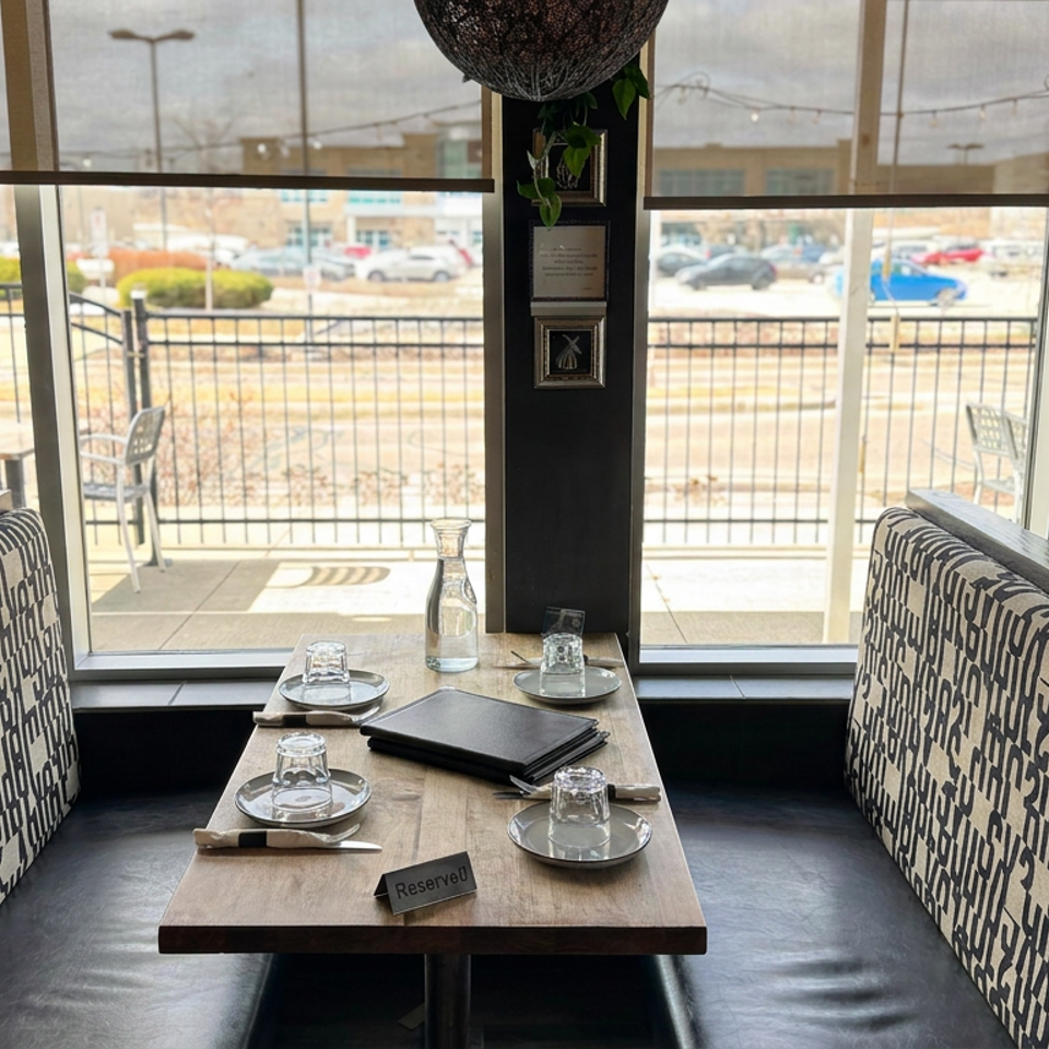 Restaurant booth with patterned upholstery, set table, reserved sign, and sunny outdoor patio visible through large windows.